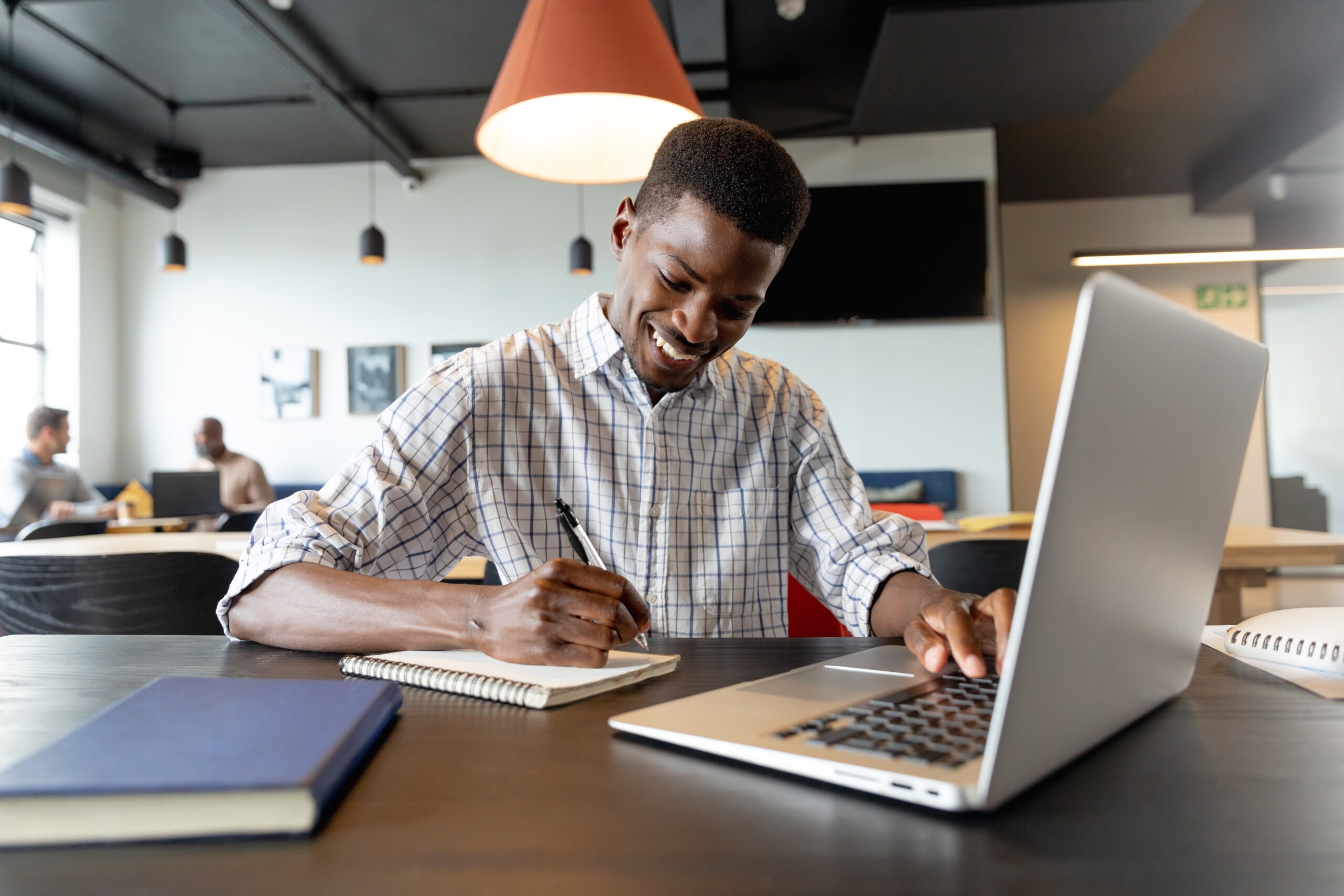 Smiling,Young,African,American,Businessman,Writing,In,Diary,And,Using