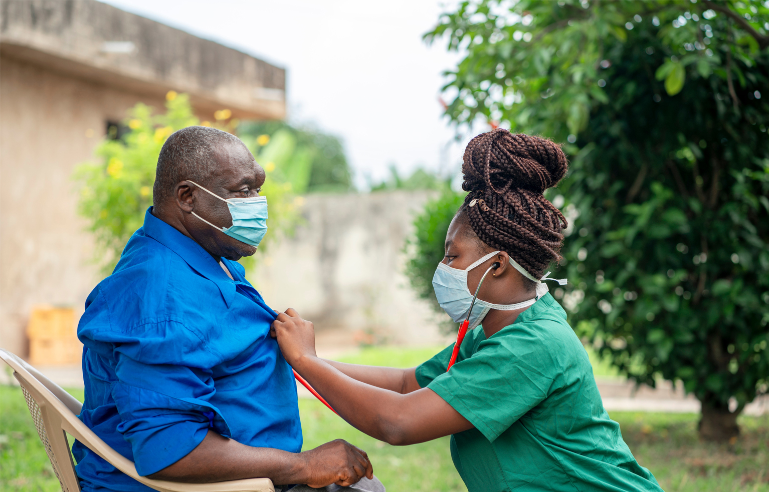 image of an aged African man being checking up by a health worker-young black nurse wearing a face mask taking care of an old man- health worker at home service